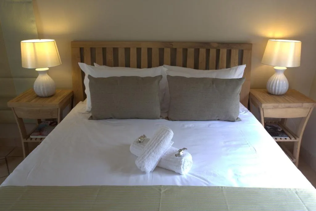 Neatly made bed with grey pillows, white linens, and fresh towels