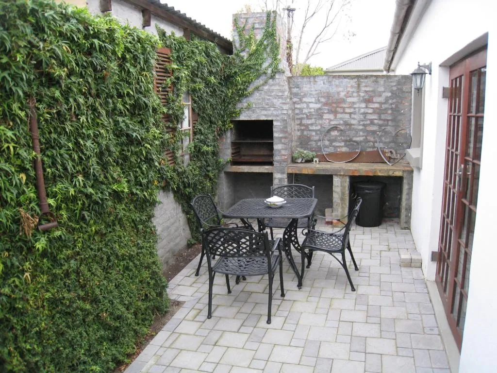Outdoor patio with dining table, chairs, and built-in braai area surrounded by ivy