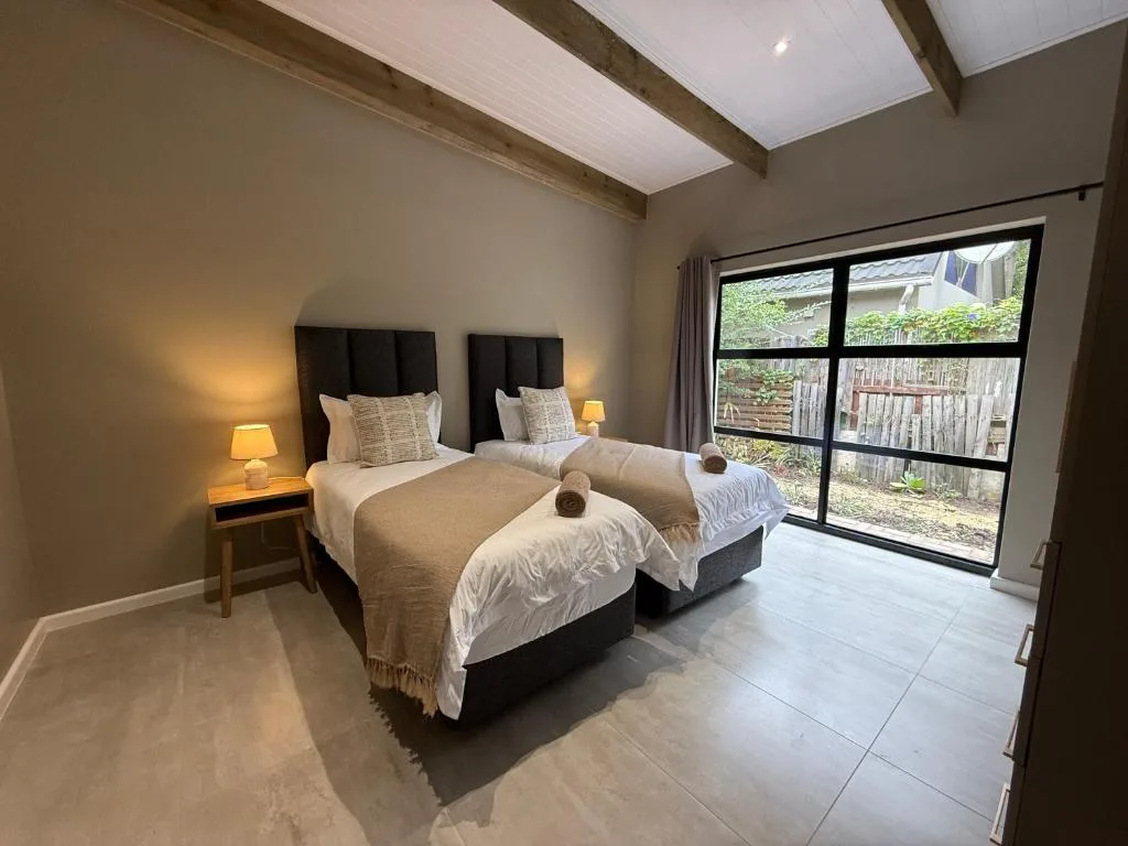 Twin beds with black headboards, warm lighting, and garden views through glass doors