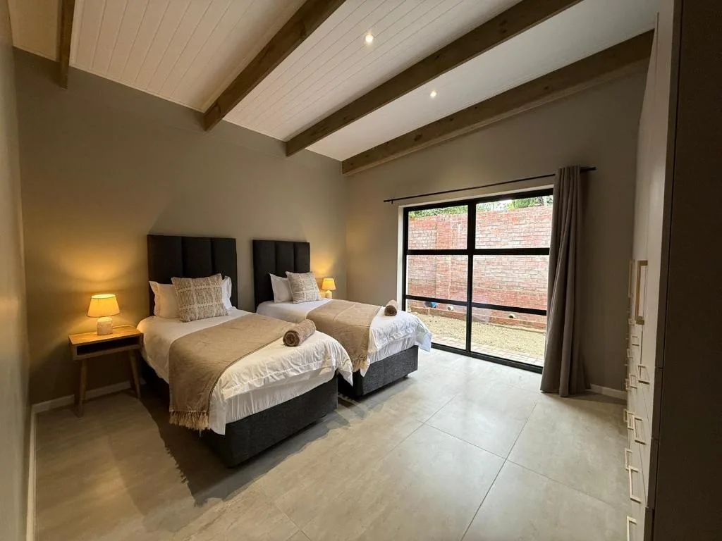 Twin bedroom with black headboards, warm lighting, and modern ceiling beams