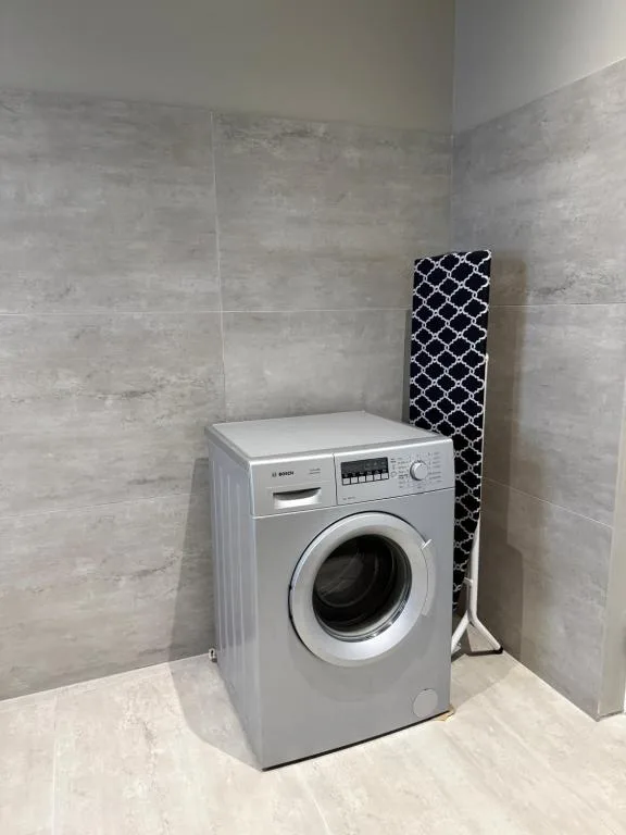 Modern washing machine in tiled utility room with ironing board