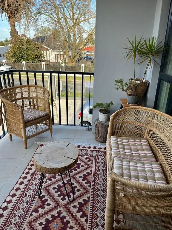 Outdoor balcony with wicker chairs, potted plants, and garden views