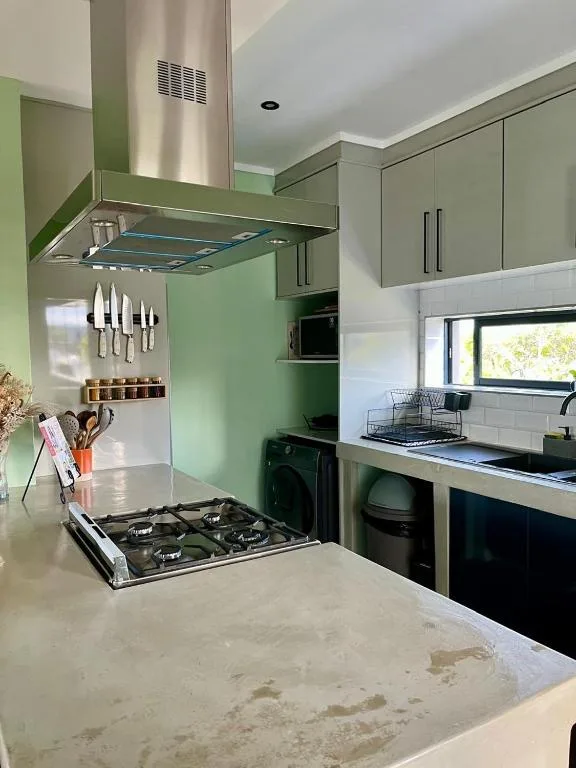 Modern green kitchen with gas cooktop, stainless steel hood, and white countertops