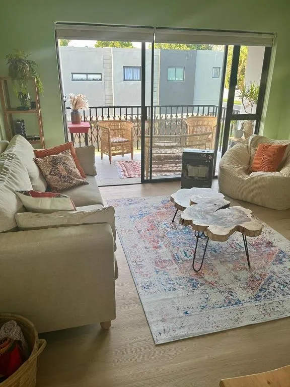 Bright green lounge with cream sofas, patterned rug, and glass doors opening to deck