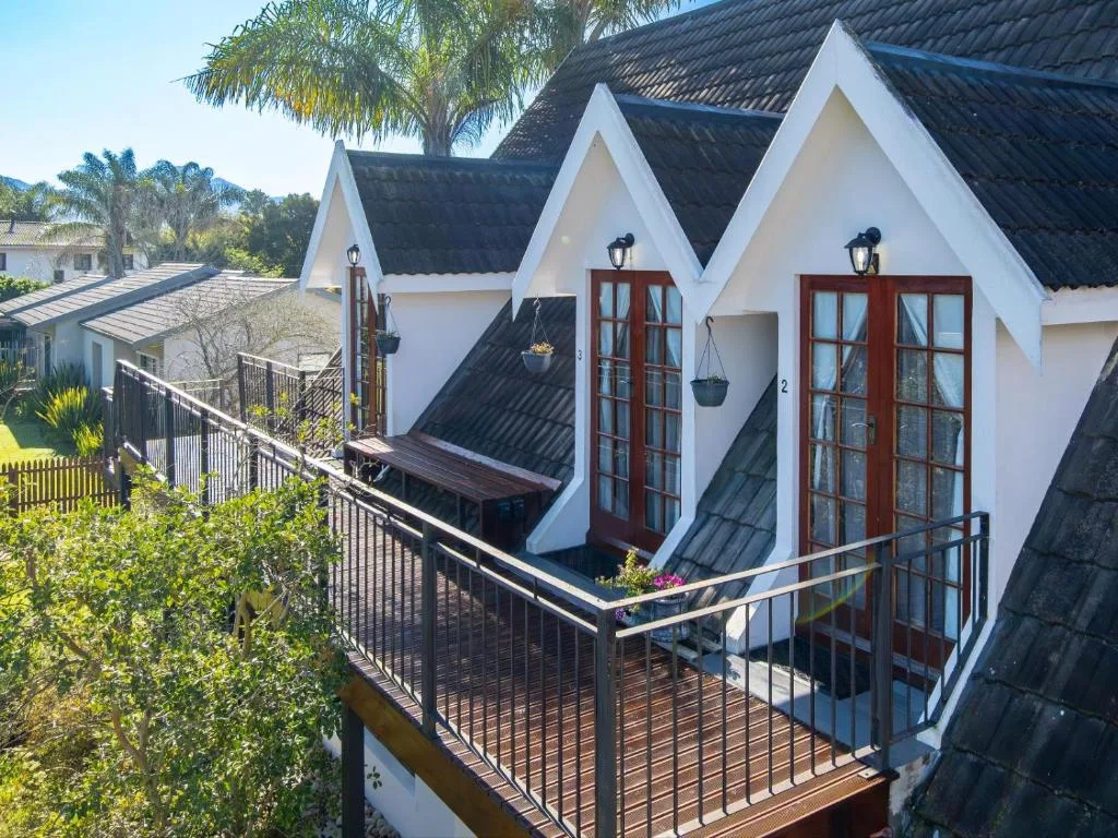 White cottage units with dark pitched roofs and red doors overlooking lush gardens