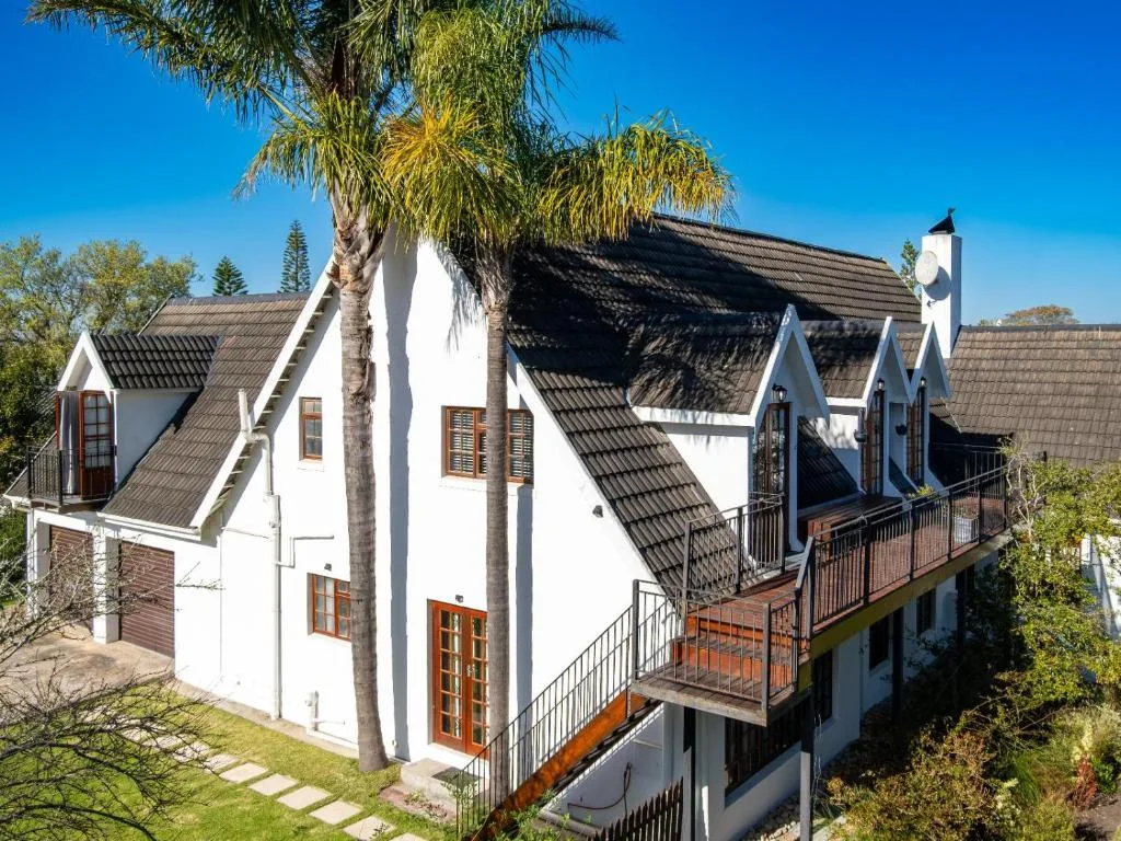 White cottage with dark tile roof and palm tree in garden