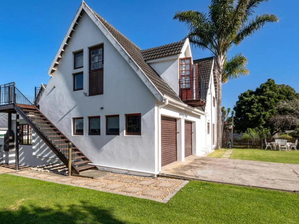White cottage with brown trim, palm trees, and manicured lawn under clear sky