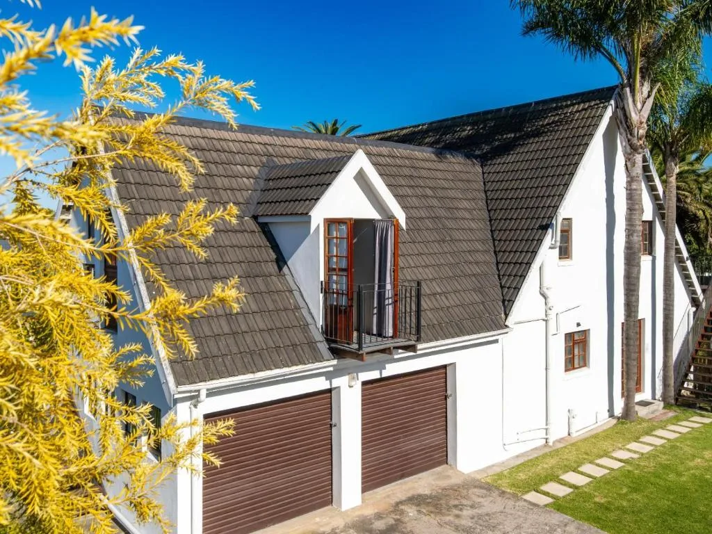 White house with dark tiled roof and wooden garage doors, sunny day