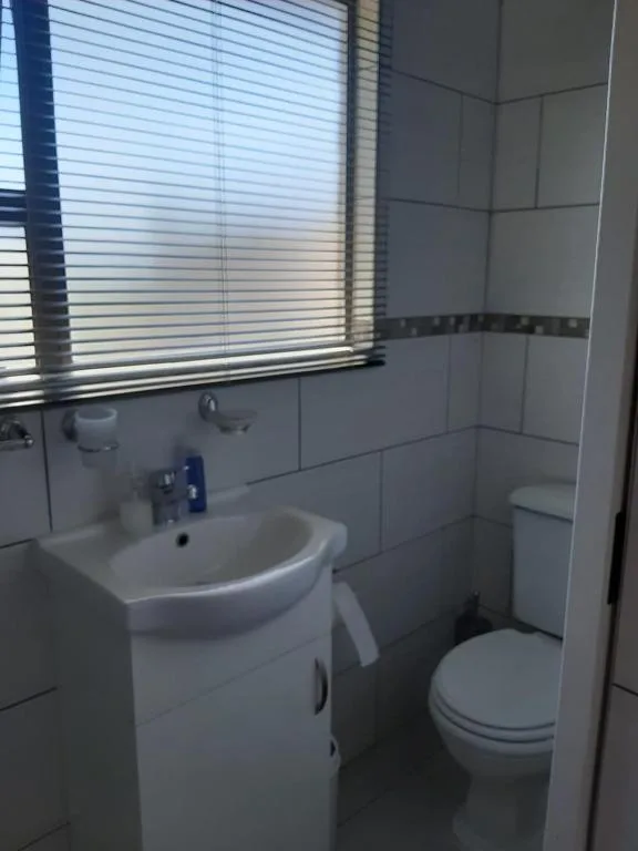 Compact bathroom with white sink vanity, toilet, and window with blinds
