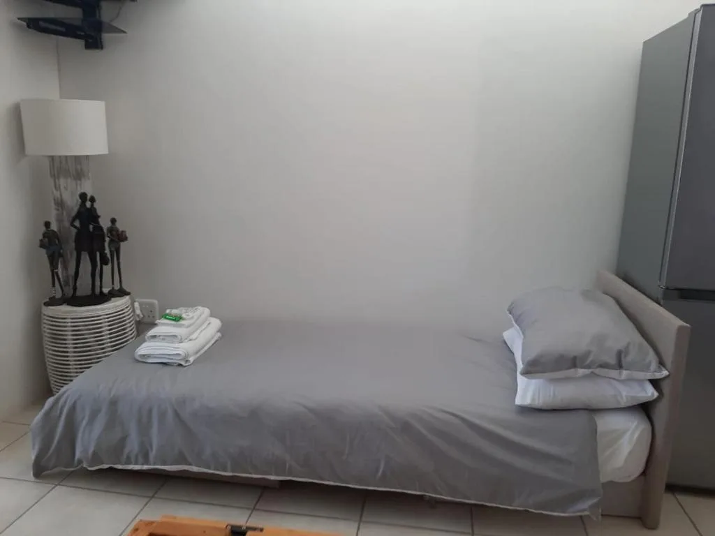 Single bed with gray bedding, pillows, and folded towels on bedside table