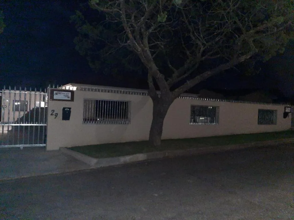 Modern beige bungalow with gated entrance and mature tree at night