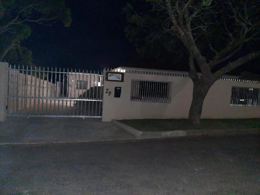 Modern single-story property entrance with metal gate and security fence at night