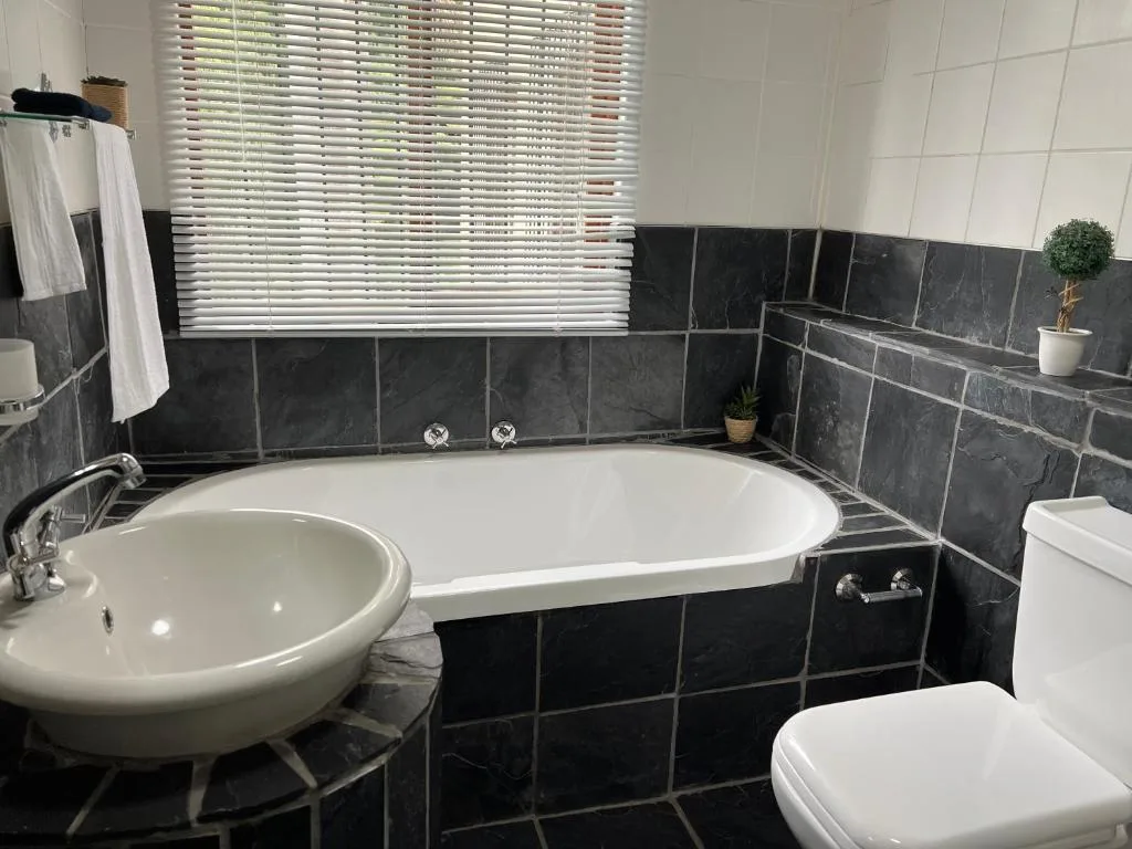 Modern bathroom with black tile walls, white bathtub, round sink, and window blinds
