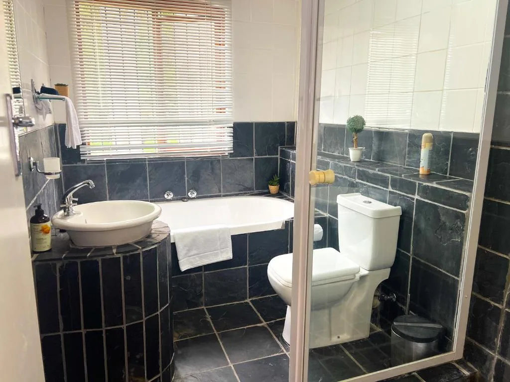 Modern bathroom with round sink, bathtub, toilet, and dark tile walls