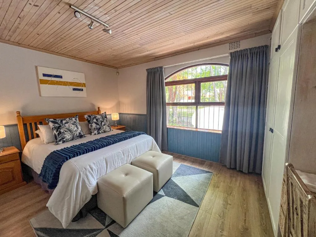 Bright bedroom with queen bed, wooden ceiling, and large window overlooking garden