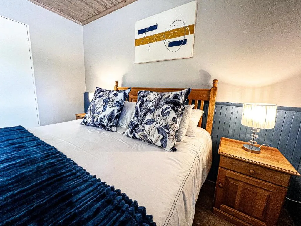 Spacious bedroom with queen bed, patterned pillows, wooden headboard, and bedside lamp