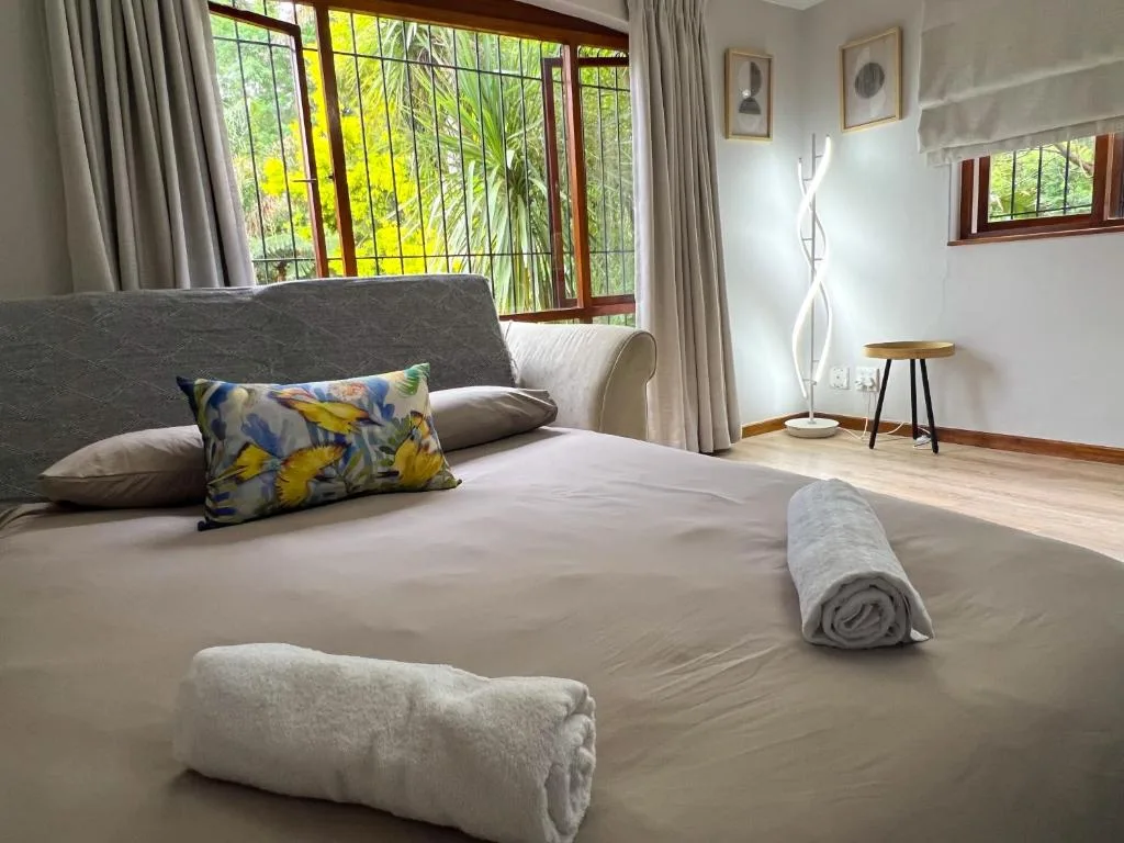 Bright bedroom with queen bed, colorful pillow, rolled towels, garden views