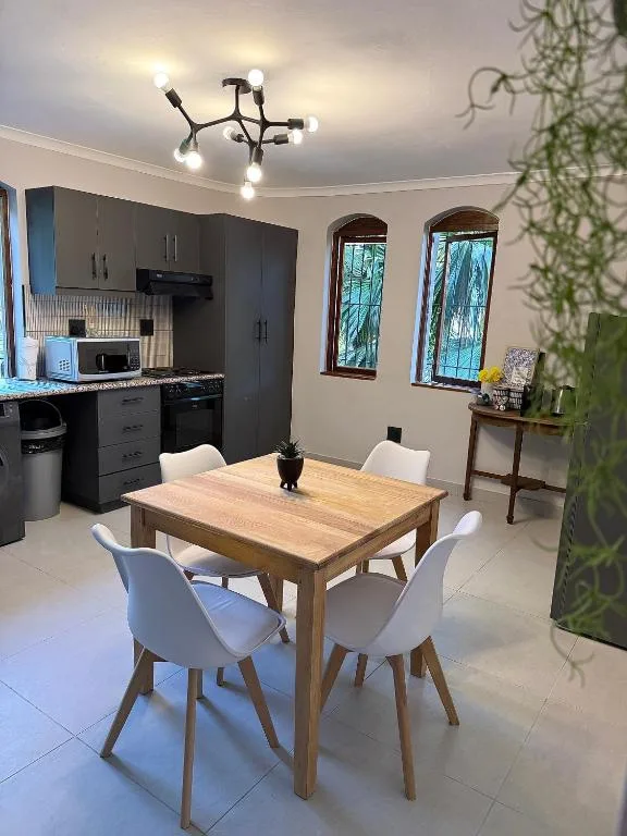 Modern dining area with wooden table and white chairs, black kitchen in background