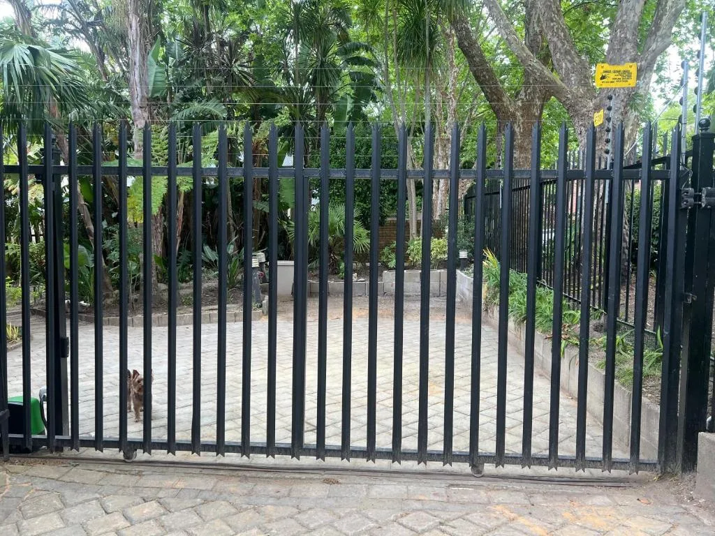 Black metal security gate entrance with mature trees and manicured grounds