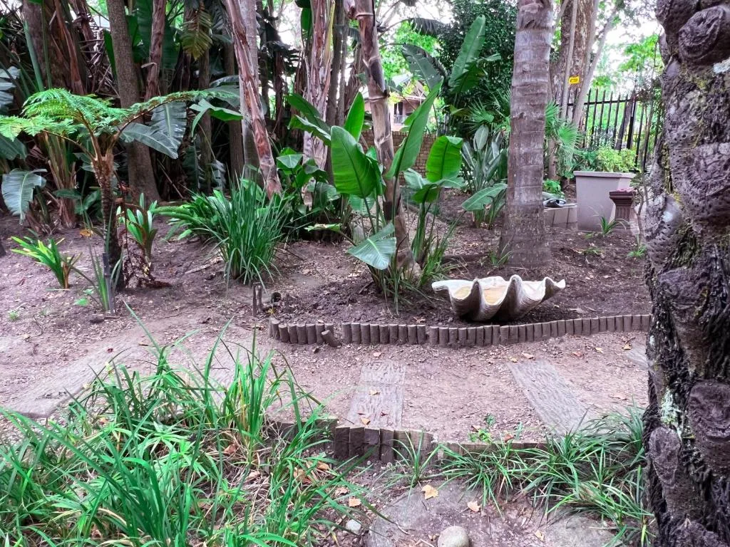 Lush tropical garden with tall trees, banana plants, and decorative seating area