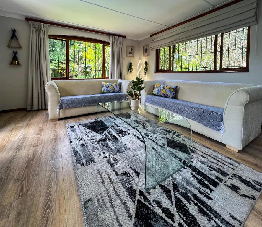 Bright living room with two cream sofas, glass table, and garden views