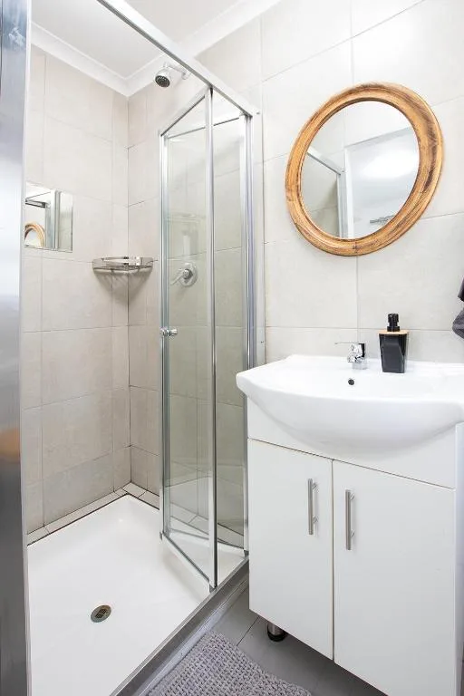 Modern white bathroom with shower enclosure and round wooden mirror