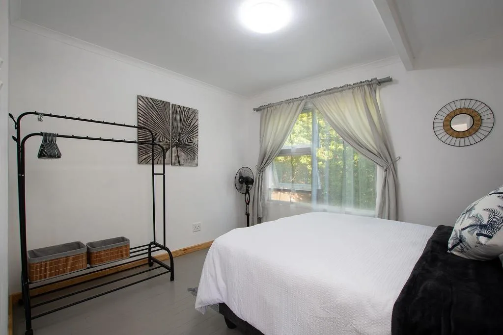 Bright bedroom with white bedding, black metal frame bed, and garden views through curtains