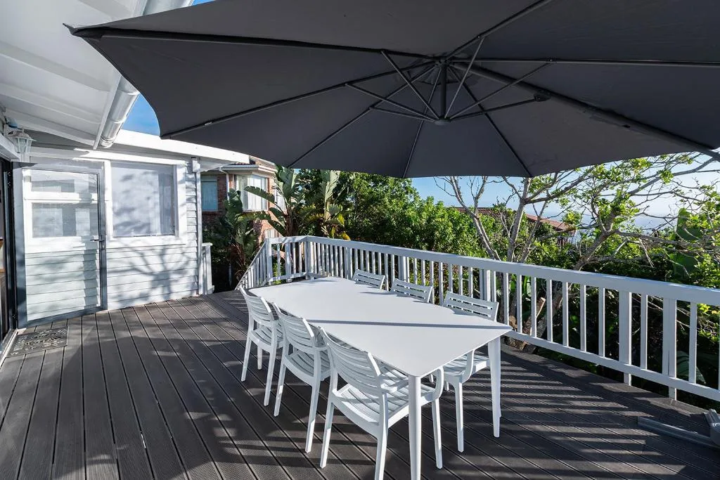 Spacious deck with dining table, white chairs, and black umbrella