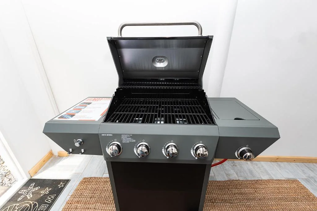 Black gas braai grill with four burners and open lid indoors