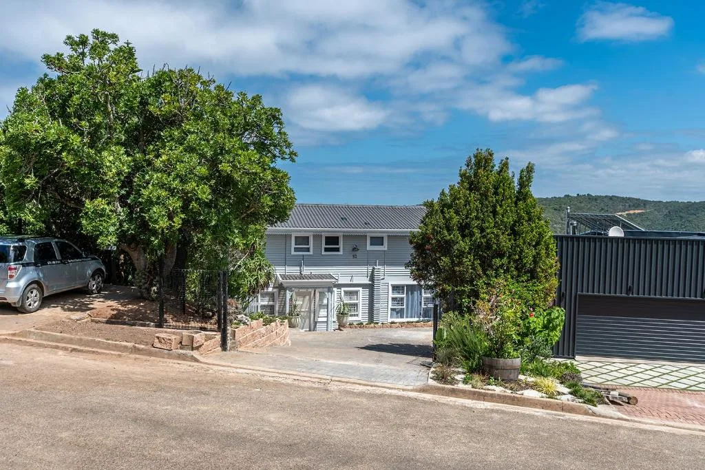 White two-story house with mature trees and parked vehicle on driveway