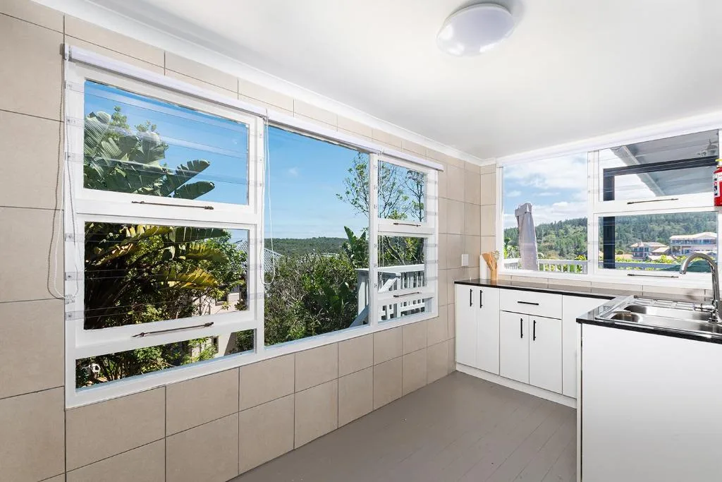 Modern kitchen with white cabinetry and expansive windows overlooking garden views