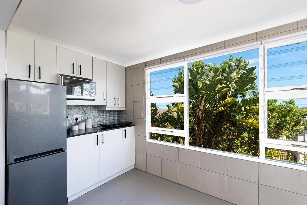 Modern kitchen with white cabinetry, stainless steel fridge, and garden views through large windows