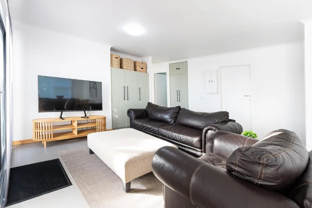Modern lounge with leather sofas, TV on wooden stand, and white storage cabinetry