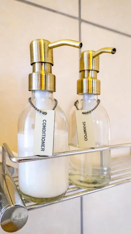 Bathroom shelf with brass pump dispensers for conditioner and shampoo