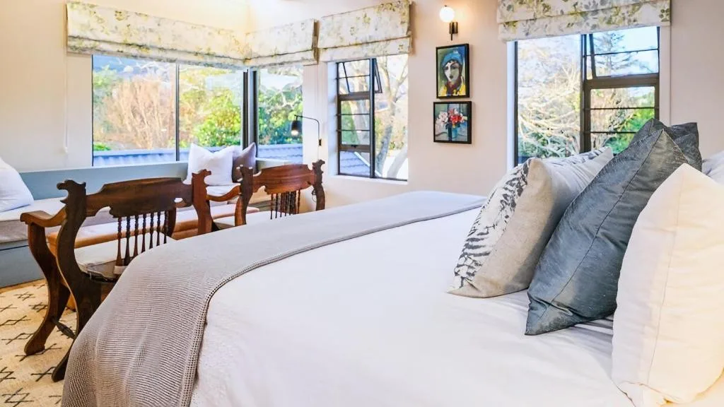 Spacious bedroom with queen bed, wooden chairs, and garden views through large windows