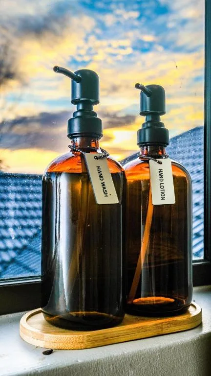 Amber glass soap dispensers with labels on wooden tray by window