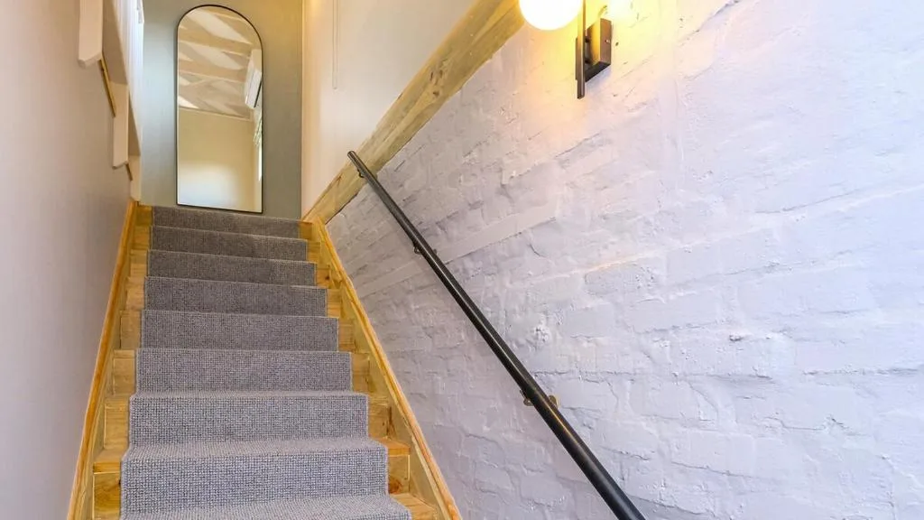 Interior staircase with gray carpet and wooden handrail leading upward