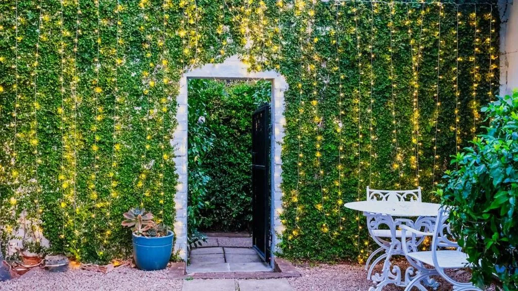 Lush green ivy-covered facade with black door entrance and white garden furniture