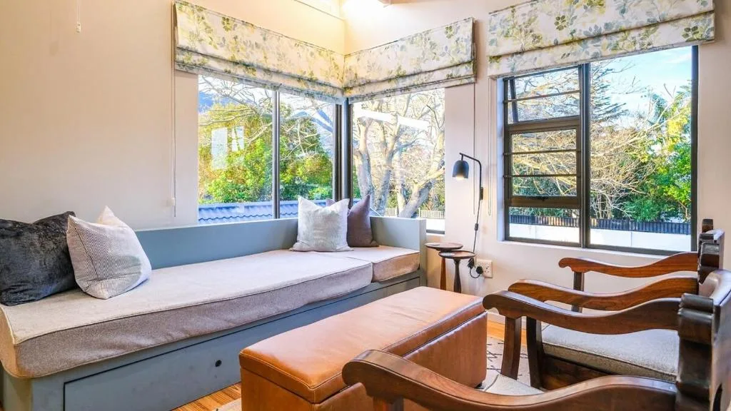 Bright lounge with window seat, cushions, and wooden chairs overlooking garden