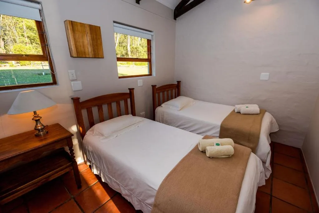Twin bedroom with wooden beds, white linens, rolled towels, and natural light from windows