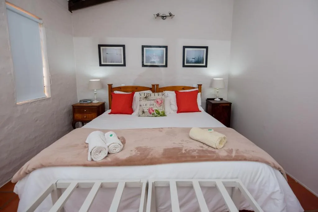 Bright bedroom with wooden bed frame, red pillows, framed artwork, and fresh towels