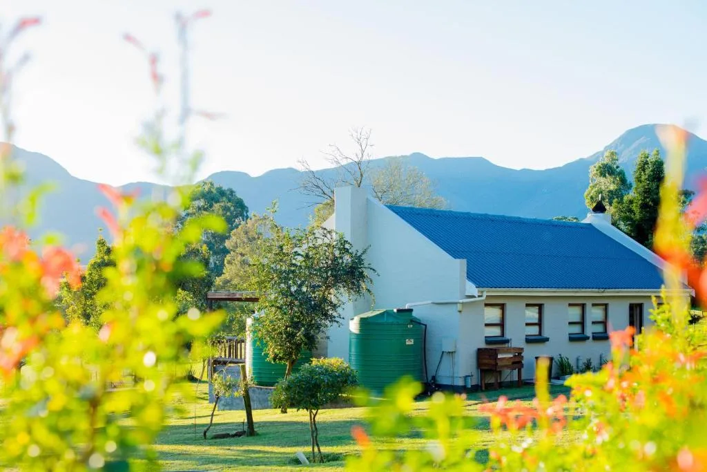White cottage with blue roof and green water tanks, mountain backdrop