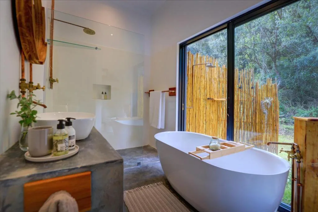 Modern bathroom with freestanding white tub and vanity overlooking garden