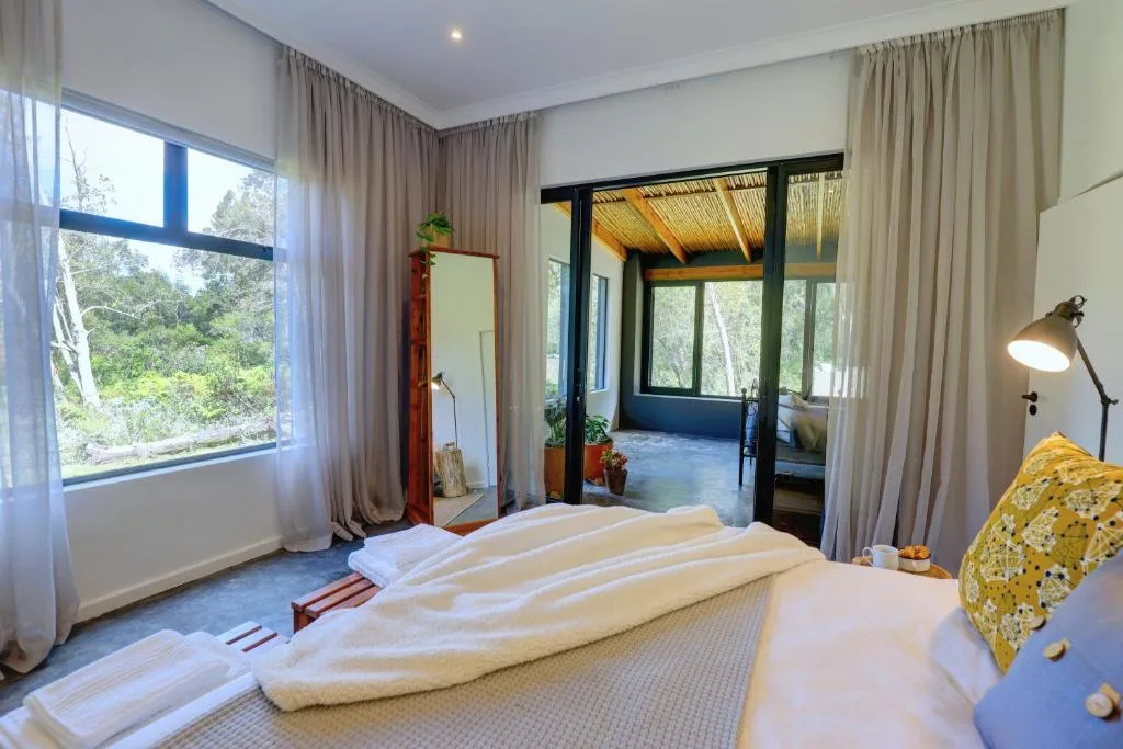 Modern bedroom with large bed, forest views through windows, and contemporary furnishings