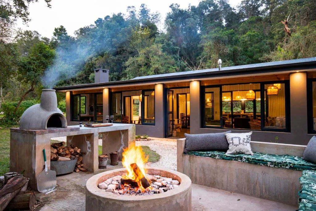 Outdoor braai area with firepit, pizza oven, seating, and modern accommodation