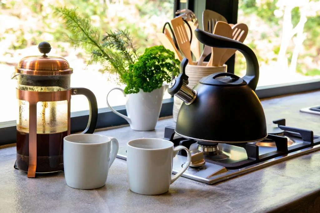 Kitchen countertop with coffee press, kettle, mugs, and utensils