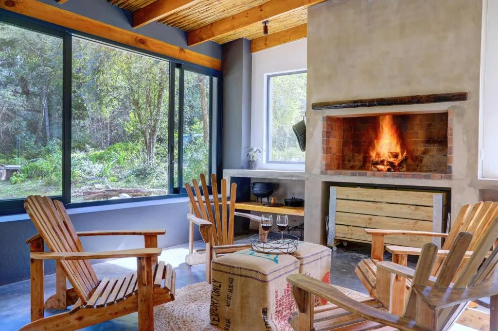 Spacious lounge with fireplace, wooden beams, and forest views through large windows