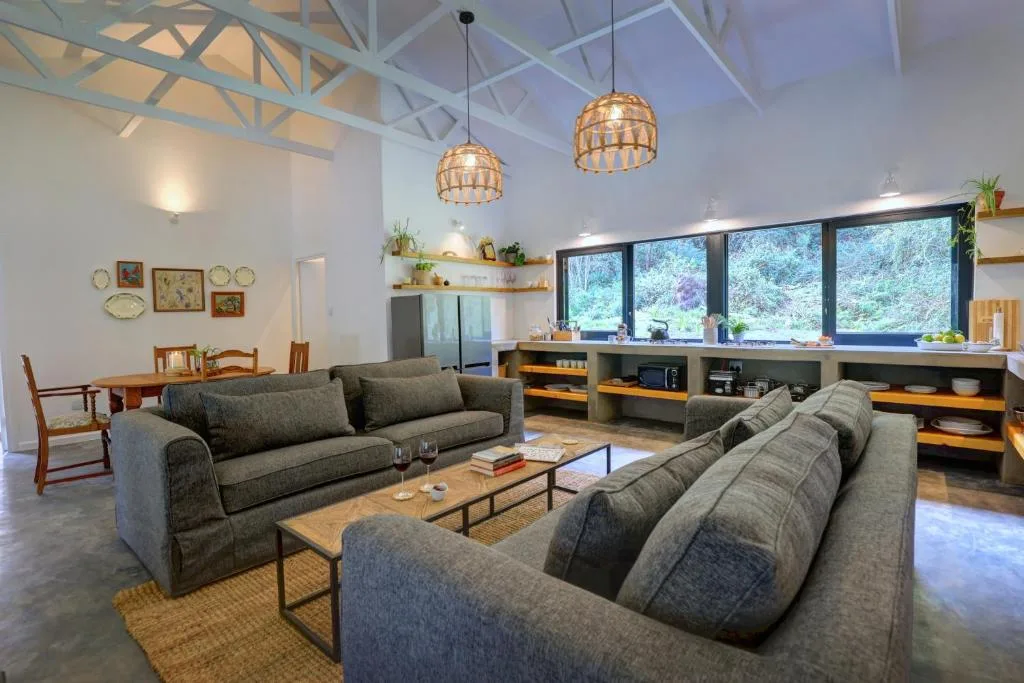 Spacious open-plan lounge with two grey sofas, pendant lights, and garden views