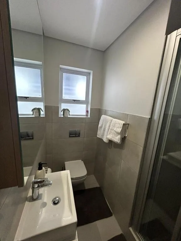 Modern bathroom with white vanity sink, toilet, and shower enclosure