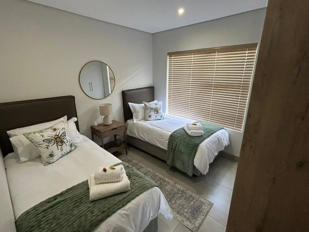 Twin bedroom with white linens, green throws, and round mirror